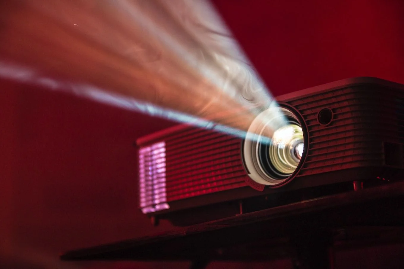 Projector emitting light beam, dark red background.